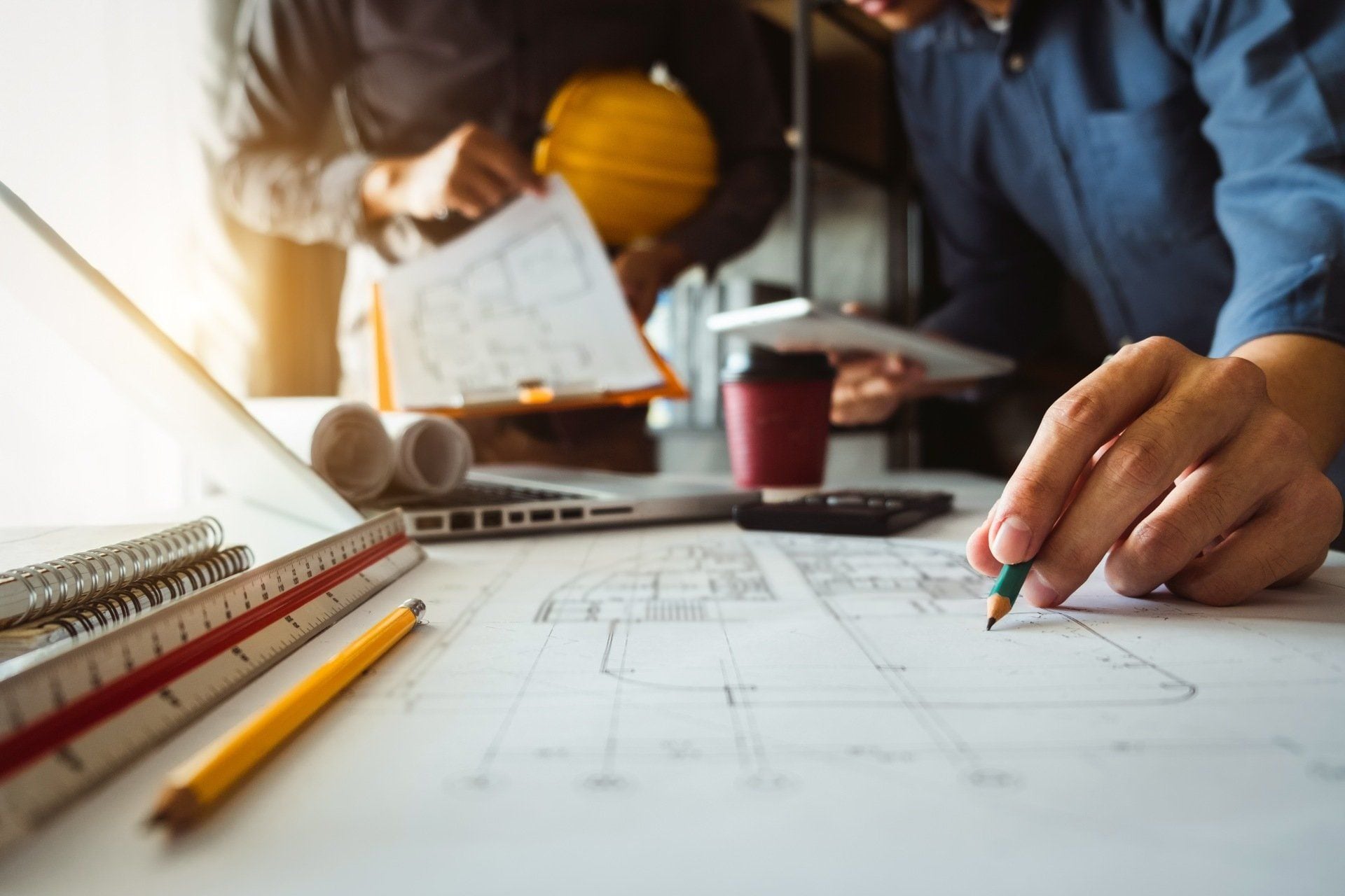 Mano che traccia una linea su un disegno tecnico, accanto a squadra e matite