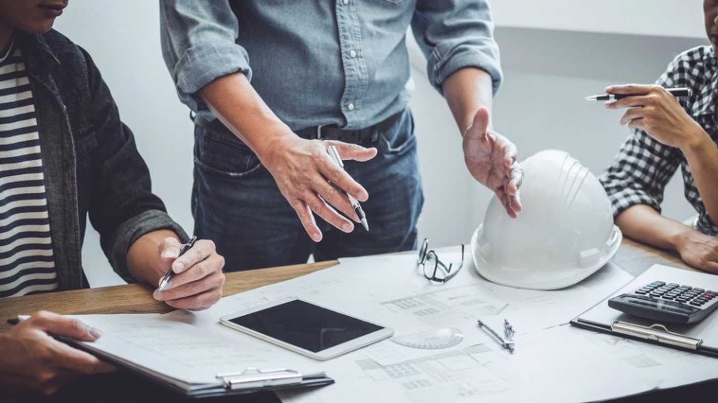 Riunione di lavoro attorno a un tavolo con planimetrie ed elmetto da cantiere